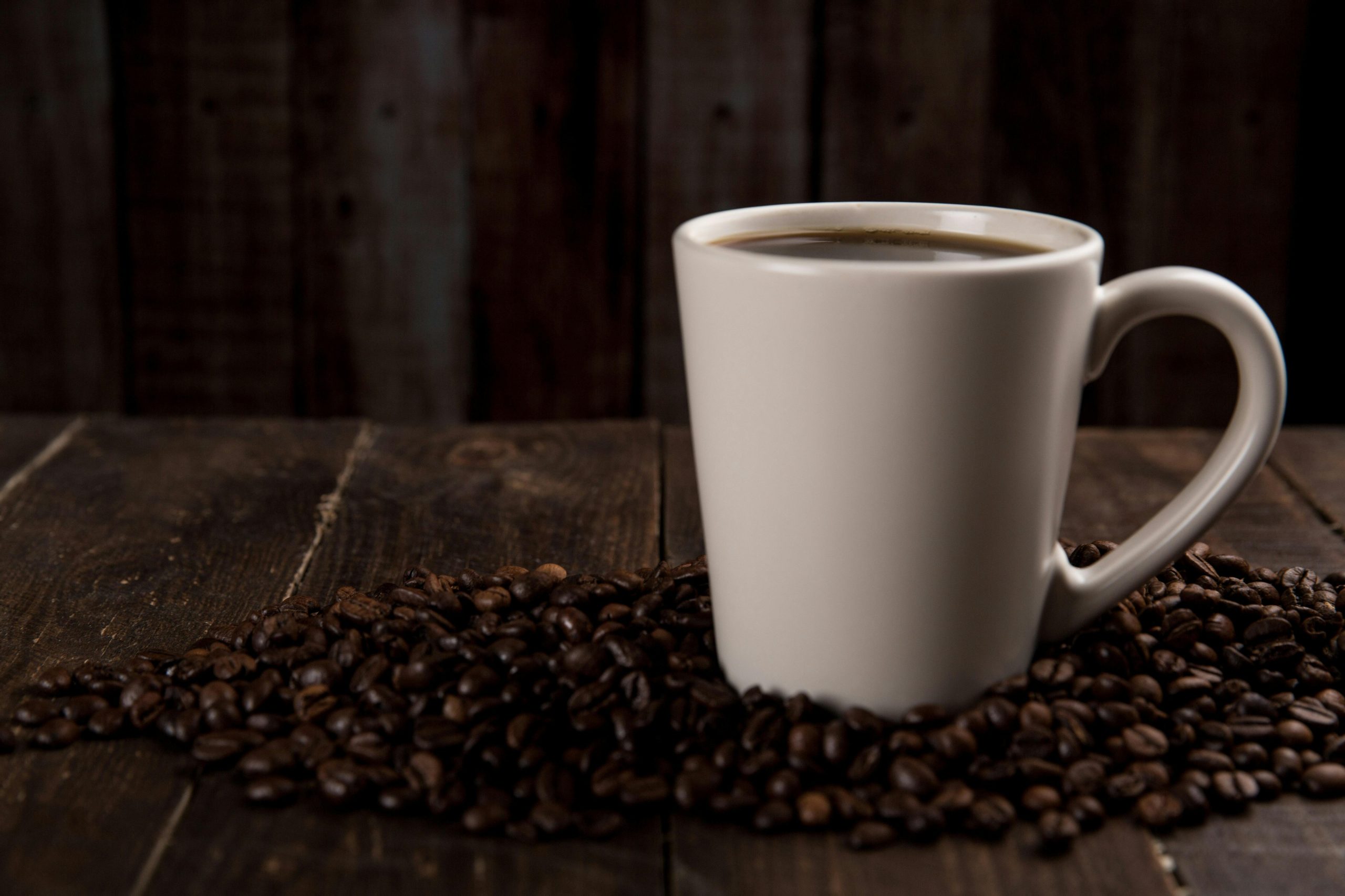 Rooms A rustic ceramic mug filled with hot coffee, surrounded by coffee beans on a wooden table.